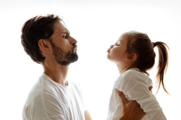 Parenthood. Family. Love. Dad is holding his little daughter in his arms. Both are making faces at each other. On white background