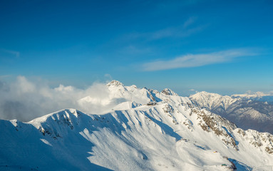 Fototapeta na wymiar Beautiful snowy ridge of caucasus mountains under clear blue sky in Krasnaya Polyana, Sochi, Russia.