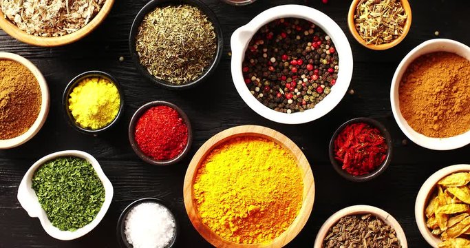 From above view of many bowls with spices of different kind on black wooden background
