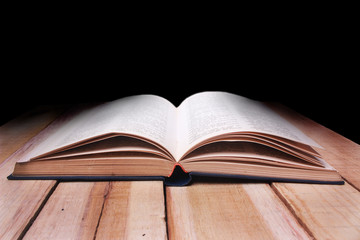 Opened Book on Wooden Table Against Black Background