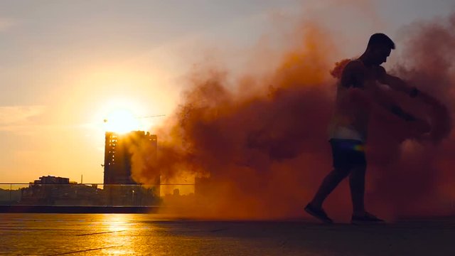 Young man hoding colored smoke, walking and finishing show. Slowmotion.