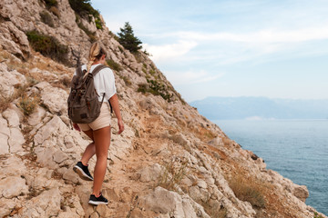 Hiker girl with backpack hiking on trail along sea bay