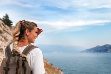 Hiker girl with backpack hiking on trail along sea bay and looking at landscape