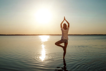 Fototapeta na wymiar Young girl silhouette, yoga on nature, on a background of a lake and beautiful sunset. Fresh air, healthy way of life, pleasure, pacification.