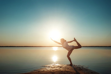 Fototapeta na wymiar Young girl silhouette, yoga on nature, on a background of a lake and beautiful sunset. Fresh air, healthy way of life, pleasure, pacification.