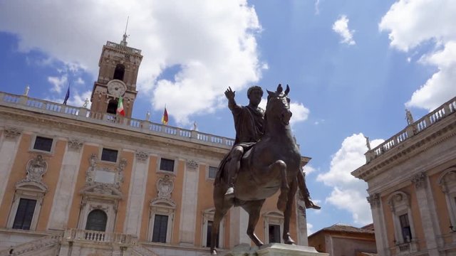 Bronze statue of Emperor Marcus Aurelius on horse on Capitol Hill in Rome, Italy in slow motion. Piazza del Campidoglio in summer day. Italian and European Union flags on background