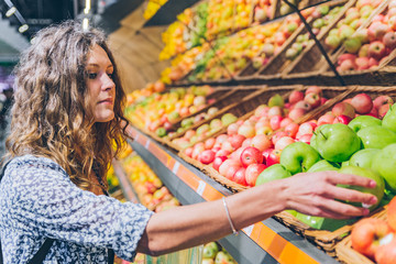 young adult woman choosing apples in grocery store