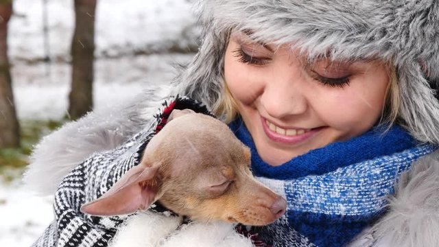 Young woman playing with her dog, pinscher ratter prazsky krysarik, outdoor during winter weather. Female hugging with love her puppy