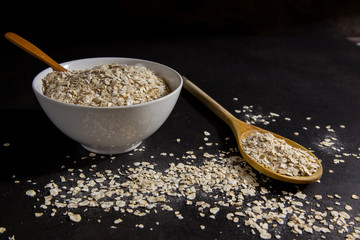 Saludables copos de avena en un cuenco y copos de avena esparcidos por la mesa