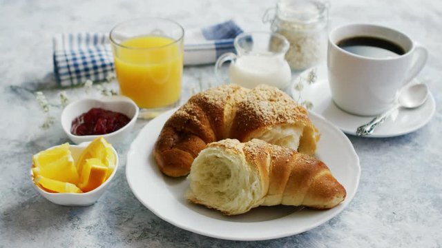 Torn soft and delicious croissant on white plate served with coffee and orange juice and marmalade on marble table