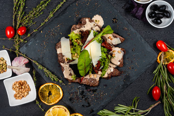 Meat veal salad with creamy sauce with herbs, cheese and pine nuts on a black stone plate