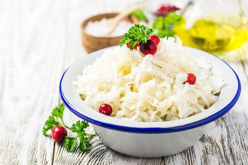 Sauerkraut with parsley, cranberries in a bowl on wooden rustic background. Selective focus, space for text.