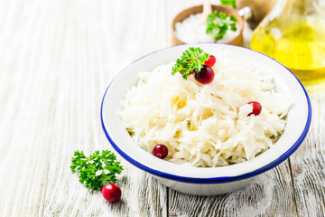 Sauerkraut with parsley, cranberries in a bowl on wooden rustic background. Selective focus, space for text.