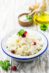 Sauerkraut with parsley, cranberries in a bowl on wooden rustic background. Selective focus, space for text.