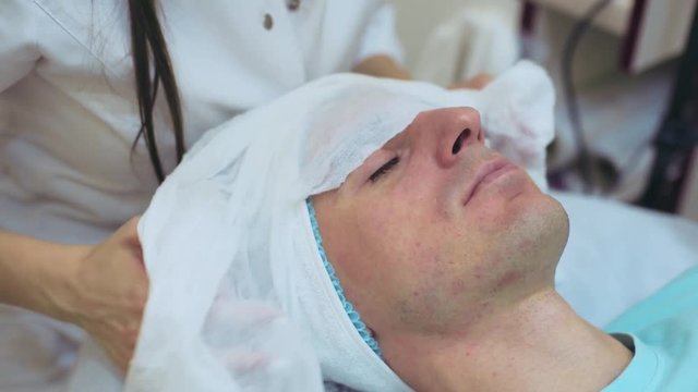 Men`s cosmetology. Young male receiving facial procedures at beauty clinic. Skin cleaning 