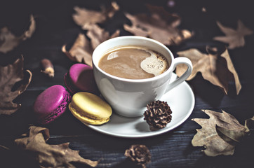 Autumn, fall dried leaves, hot steaming cup of cappuccino coffees, macaroons, cones, newspaper on wooden table background. Seasonal, evening coffee, Sunday relaxing and still life concept. Flat lay. 