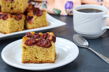 Slices of a plum pie on a plate, are located on a dark background. Piece of pie in the foreground, next to a cup of coffee