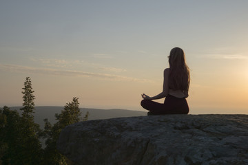 Woman meditating on the sunset in the mountains