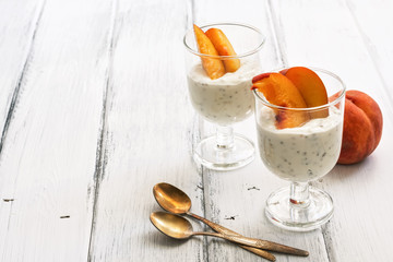 A useful breakfast, yoghurt with pieces of peach and chia seeds on a white wooden rustic table. Selective focus, copy space.