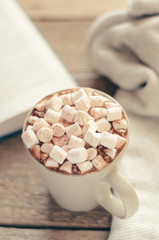 Hot cocoa with marshmallow and spices on wooden table with a gray knitted plaid. Cozy breakfast, autumn weekend.