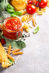 Glass jar with homemade classic spicy tomato pasta or pizza sauce with pine nuts and basil. Italian healthy food background. Copy space.