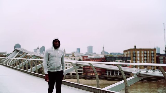 Young sporty black man runner with smart watch walking on the bridge in London.