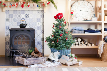 Christmas interior with decoration in rustic style. Decorated living room in cozy house. Christmas tree with red ornaments. Gifts, presents, skates are under fir tree near wood burning stove, firewood