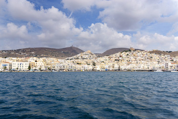 Fototapeta na wymiar Beautiful view of Ermoupolis city port on Syros island, Greece. Sunny day, dark Aegean sea, cyan sky with clouds and seafront architecture