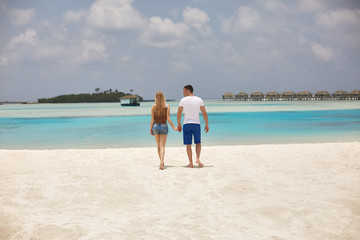 Fototapeta na wymiar Back view of couple holding hands and walking to the blue ocean lagoon on Maldives at luxury spa resort. Travel and honeymoon concept.