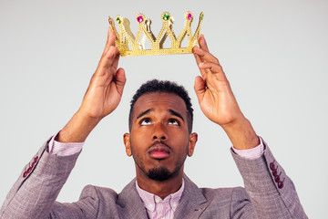 smart african american successful and rich businessman in a stylish suit and the golden crown on his head on white background in studio shot. the concept of well-deserved respect and luck © yurakrasil
