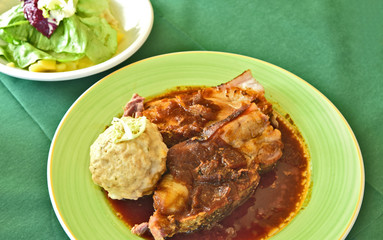 Roast pork with bread dumplings (German name is Schweinebraten mit Semmelknödel) in green dish and Green salad