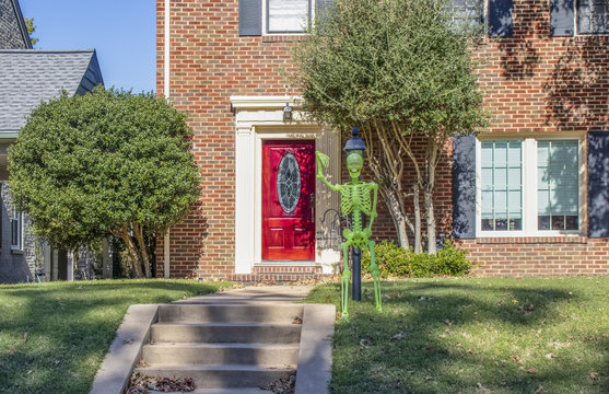 Dayglo Halloween skeleton attached to lamp post outside upscale brick house with beautiful bright red front door
