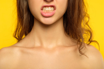 emotion expression. furious woman in rage baring her teeth. hateful scowl and hatred concept. young beautiful brunette girl portrait on yellow background.