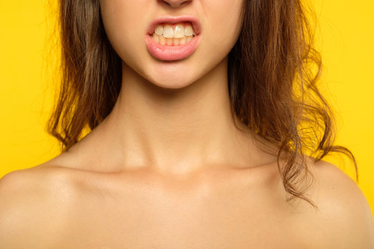emotion expression. furious woman in rage baring her teeth. hateful scowl and hatred concept. young beautiful brunette girl portrait on yellow background.