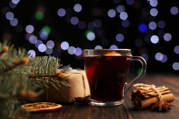 Mulled wine, gift and spices on the background of Christmas lights. On the table next to the tree.