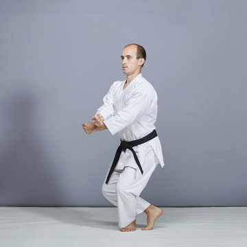 A young athlete with a black belt does formal karate exercises on a gray background