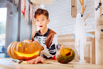 Fototapeta premium Excited boy. Cute funny boy wearing feeling skeleton costume excited while standing near carved Halloween pumpkin