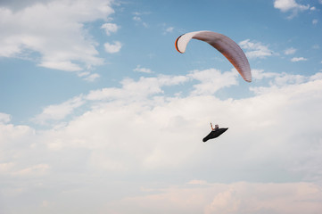 Alone paraglider flying in the blue sky against the background of clouds. Paragliding in the sky on a sunny day