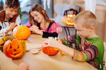 Ninja costume. Blonde-haired handsome cute boy wearing Ninja turtle costume for Halloween decorating pumpkin