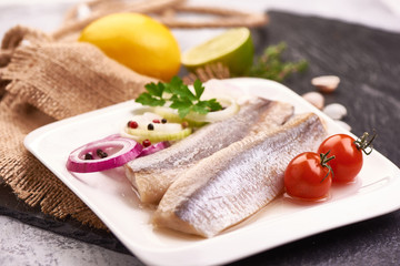 Delicious Atlantic salted herring with onion and tomatoes on the slate shale background. Rustic...