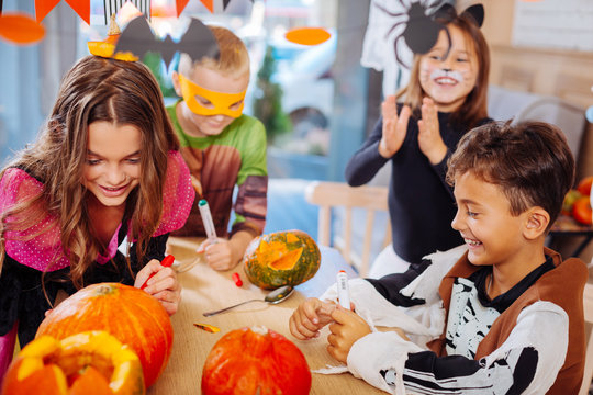 Halloween party. Four good-looking beaming children attending Halloween celebration coloring pumpkins together
