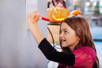 Halloween day. Beautiful cute dark-haired girl wearing pink and black dress feeling happy on Halloween day