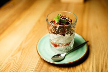 Glass bowl of ice cream dessert with chocolate and nuts close-up on wooden background with copy space