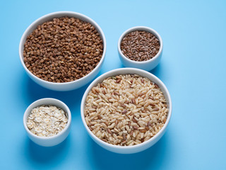 brown rice, buckwheat, flax and oat flakes in white cups on a blue background