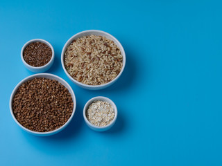brown rice, buckwheat, flax and oat flakes in white cups on a blue background