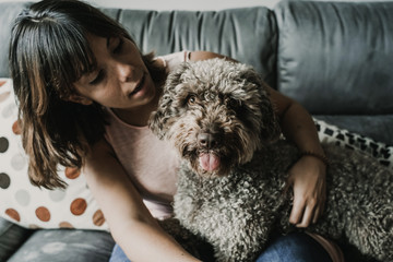 .Young and funny girl playing with her sweet spanish water dog on the sofa of her home. Pet friendly. Lifestyle.