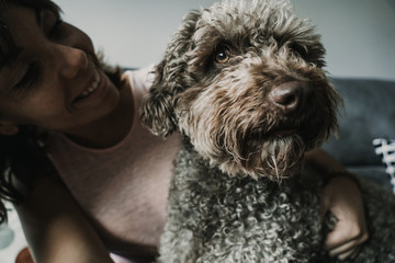 .Young and funny girl playing with her sweet spanish water dog on the sofa of her home. Pet friendly. Lifestyle.