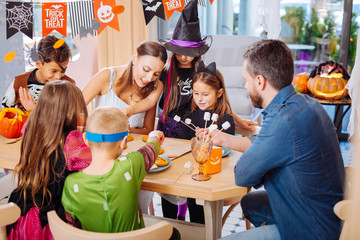 Treats and sweets. Loving parents feeling memorable while treating their children wearing Halloween costumes with sweets