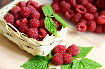 A lot of fresh Raspberry with green leaf in basket on wooden table.