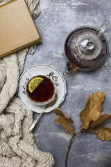 Cup with black tea and lemon and saucer, spoon, jelly in jar, maple leaves and knitted scarf near, an gray background